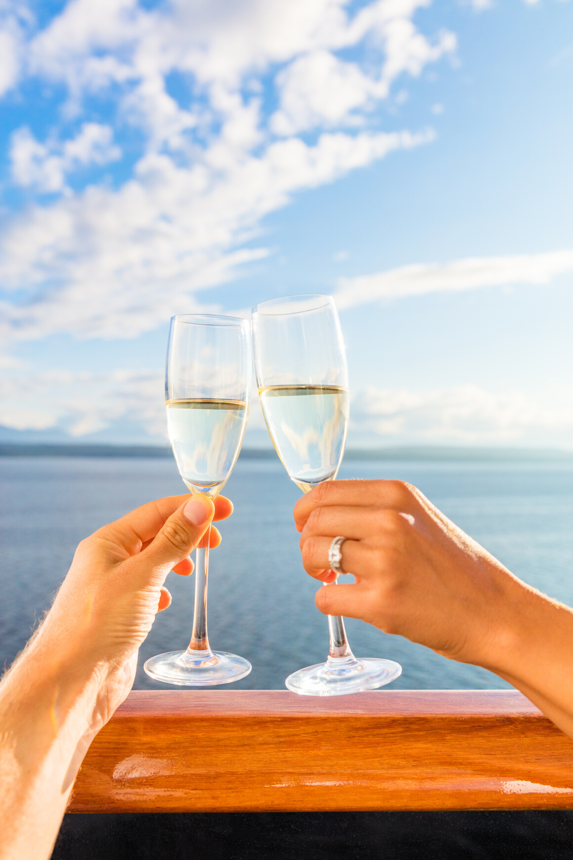 Luxury Honeymoon Cruise Couple Toasting Champagne. Travel Holiday Newlyweds Drinking with Wedding Rings Holding Glasses Doing Cheers at Sunset View of Cruise Holiday Destination
